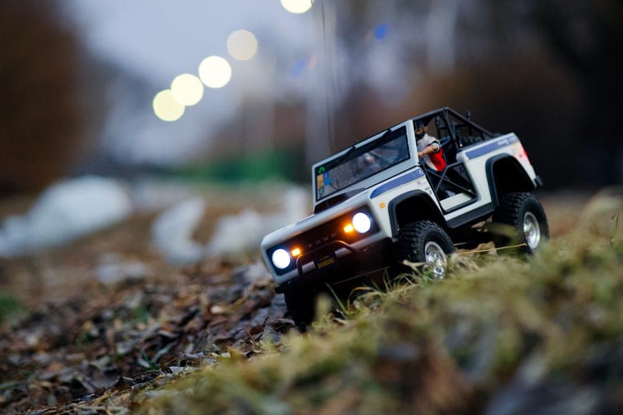 A small monster-truck-style RC vehicle on a leaf-covered path at dusk