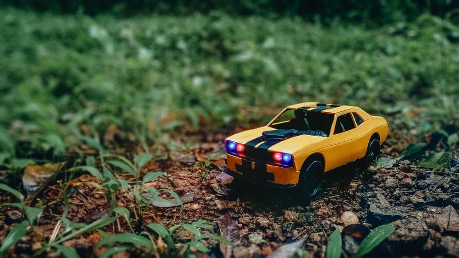 A bright toy car sitting in grass and leaves